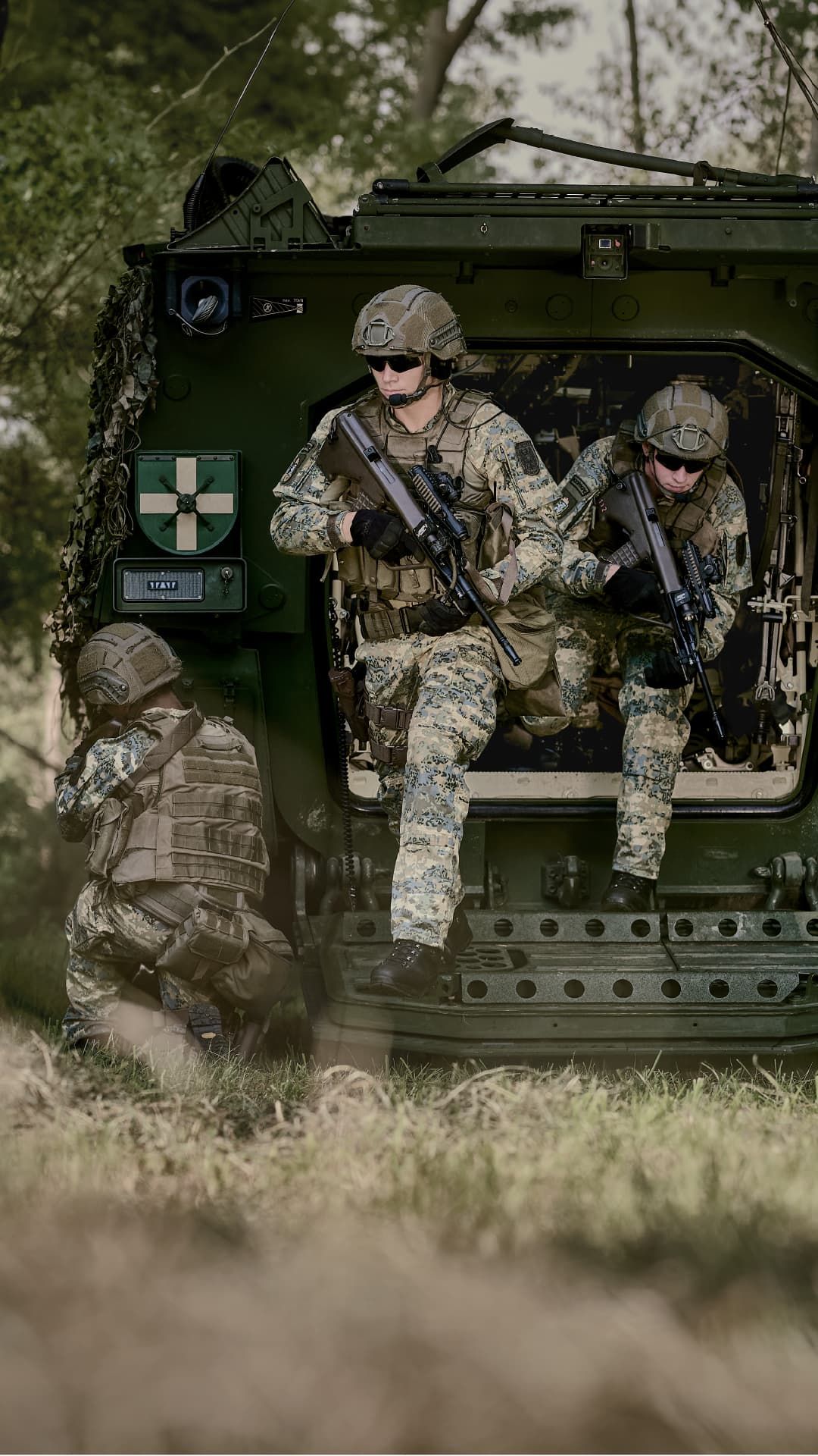 Zwei Soldaten des österreichischen Bundesheeres in Tarnuniform, einer stehend mit Gewehr, der andere kniend mit Tablet; im Hintergrund eine Drohne und eine grün leuchtende Österreich-Karte.