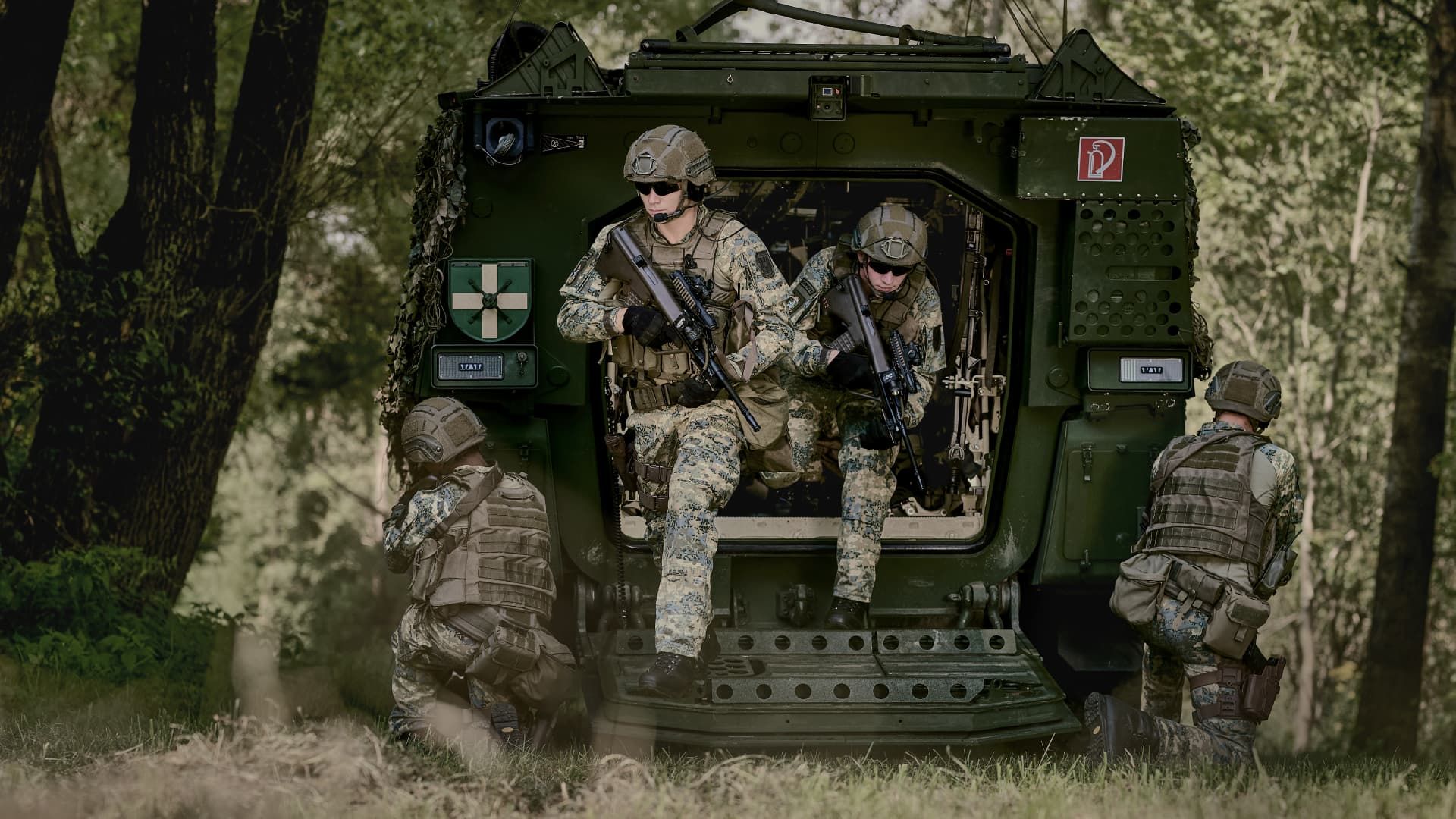 Zwei Soldaten des österreichischen Bundesheeres in Tarnuniform, einer stehend mit Gewehr, der andere kniend mit Tablet; im Hintergrund eine Drohne und eine grün leuchtende Österreich-Karte.